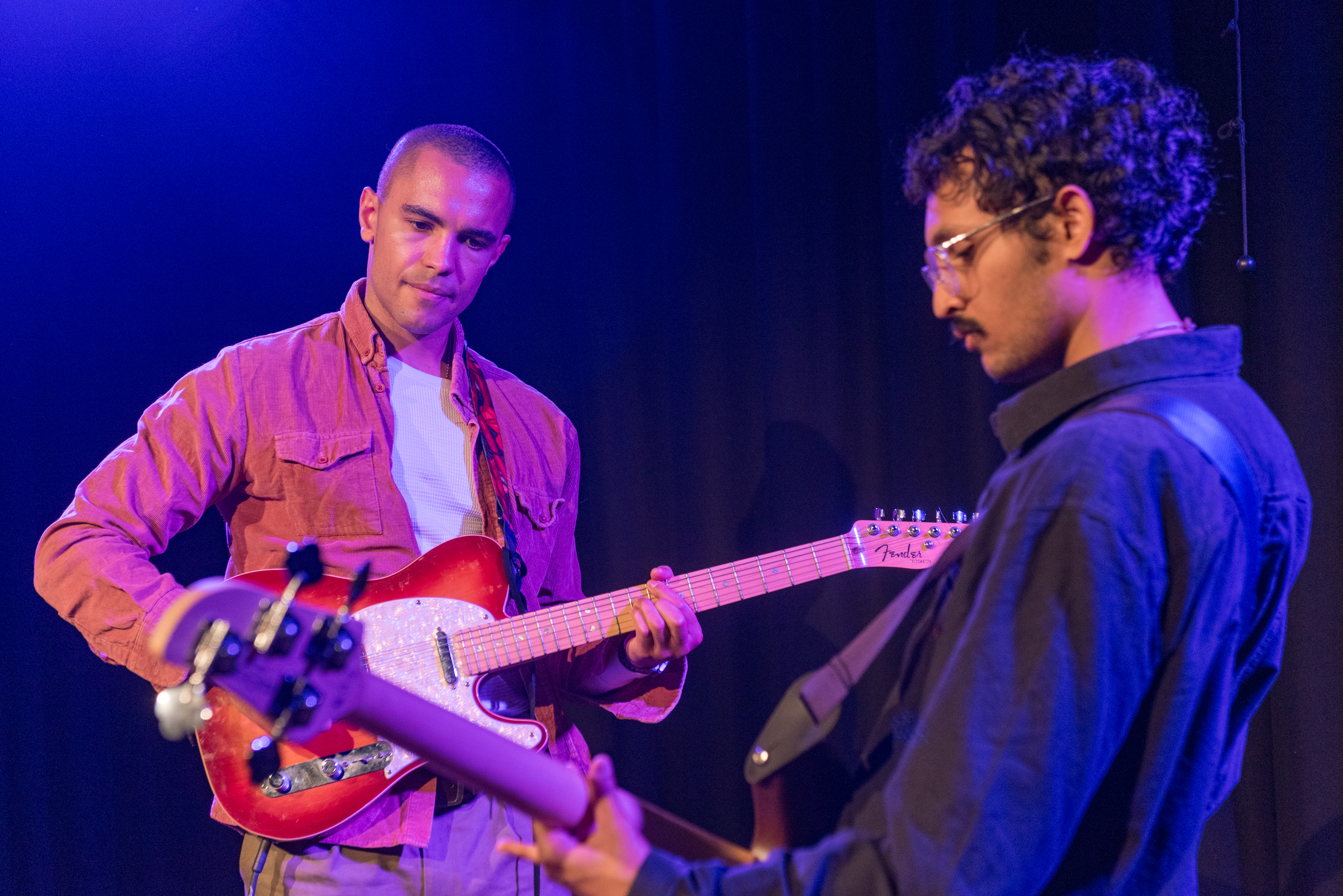Young black male playing electric guitar and young Asian male playing bass guitar on stage
