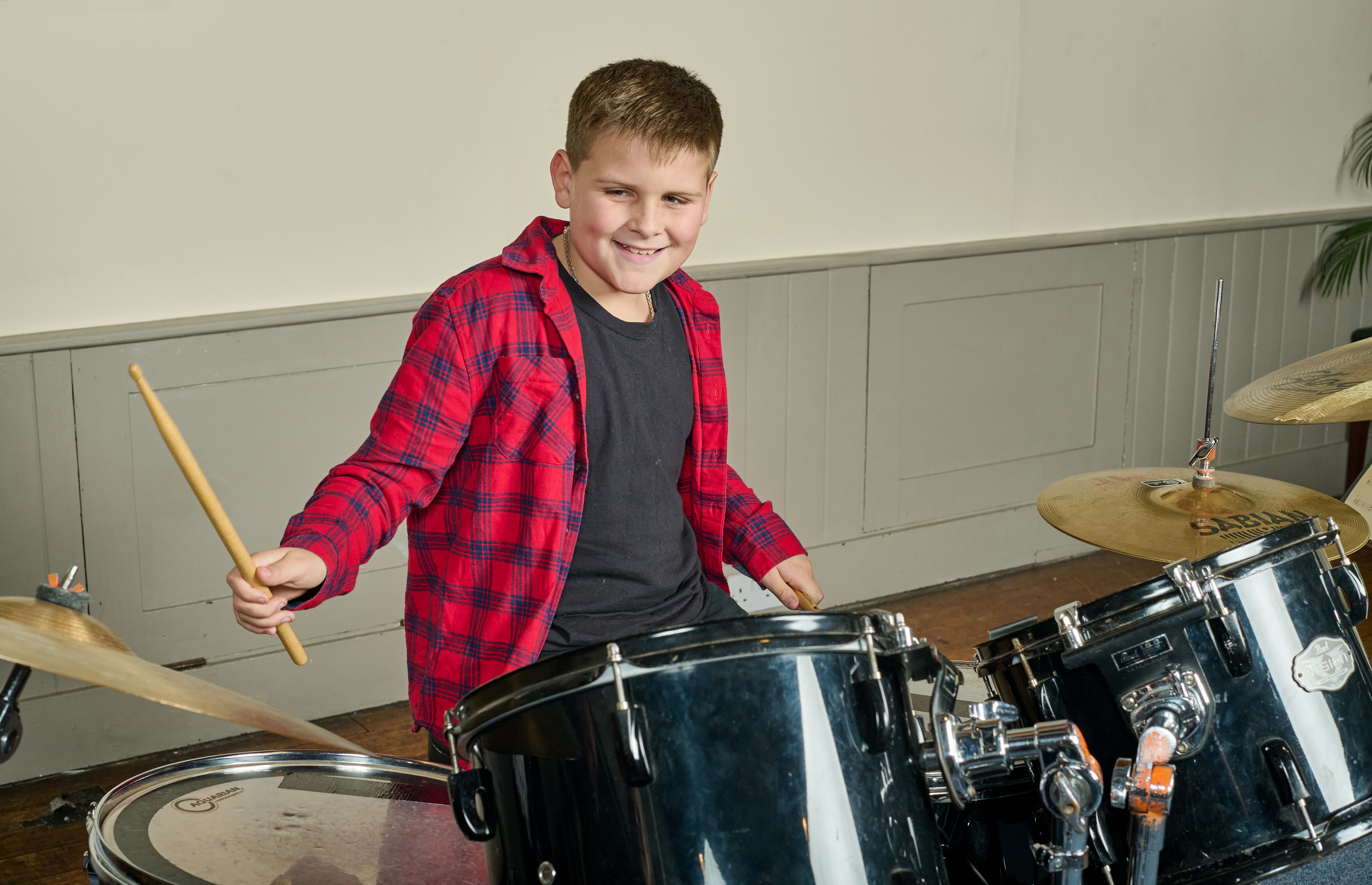 Young white male playing an acoustic drum kit whilst smiling